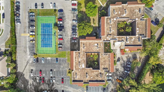 Aerial view of parking area with cars, adjacent tennis court, and buildings with rooftop features.