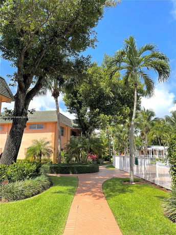 Pathway leading to a multi-story building with palm trees and manicured hedges.