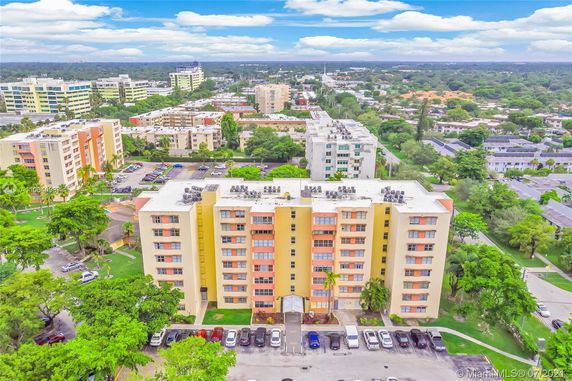 Aerial view of a multi-story residential building with parking area and surrounding greenery.