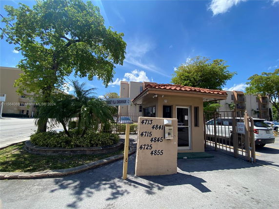 Front elevation view of a small security booth with adjacent parking area and gated entrance.