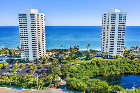 Two tall residential towers with the ocean in the background, surrounded by lush greenery and landscaped areas.