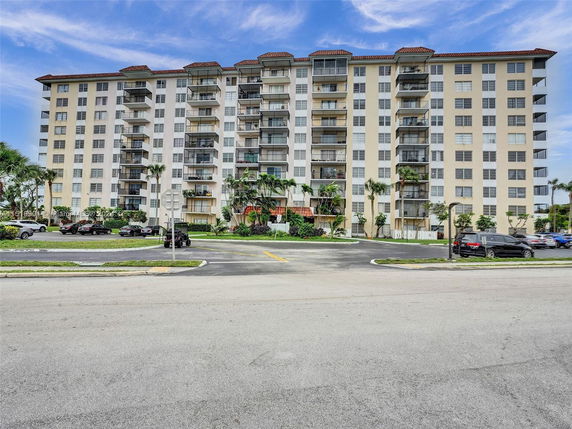 Front view of a multi-story residential building with balconies and a parking area.