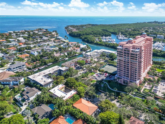 Aerial view of a coastal residential area with a tall apartment building and surrounding houses, near a body of water.