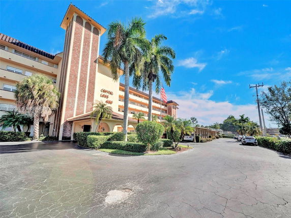 Front view of a multi-story building with palm trees and parking area.