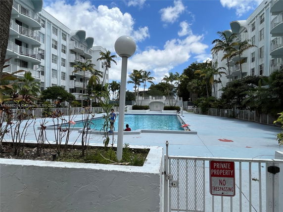 Outdoor swimming pool area in front of a multi-story residential building.