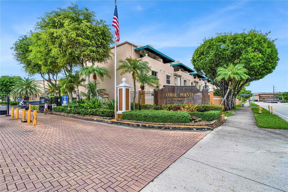 Front view of a condominium building with a sign and landscaped entrance.