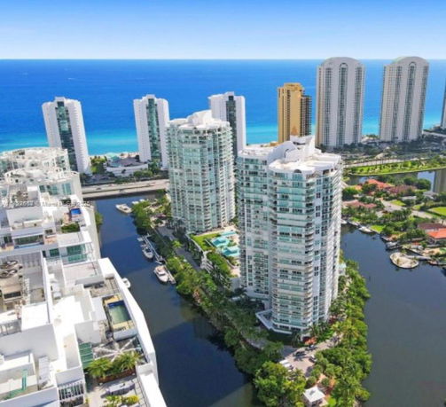 Panoramic view of multiple high-rise buildings near a waterway with ocean in the background.