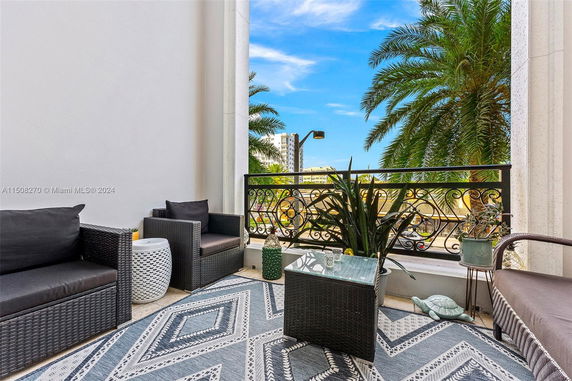 Balcony with wicker furniture and a view of palm trees and buildings.