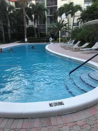 Outdoor swimming pool area with surrounding trees and a building in the background.
