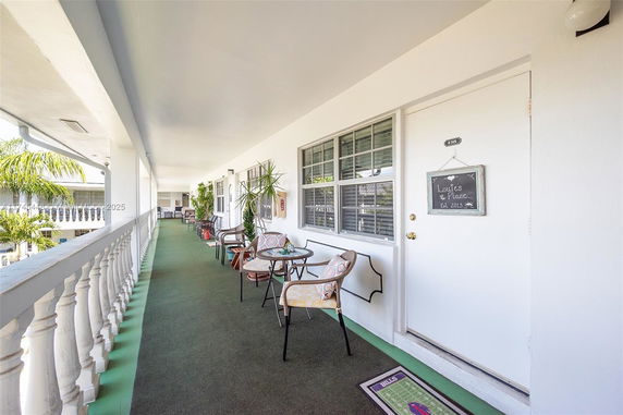 Exterior walkway of a building with chairs and small tables outside apartments.