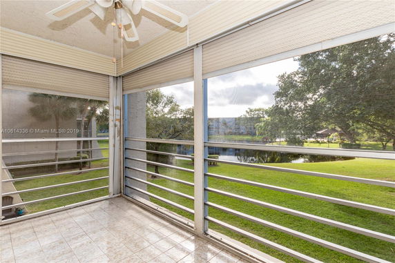 View from an enclosed balcony overlooking a grassy area and pond with trees in the background.