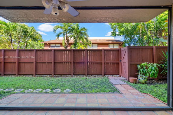 View of a fenced backyard with paving stones and a lawn, surrounded by trees.