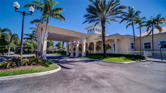 Front view of a large building with a covered entrance and multiple palm trees.