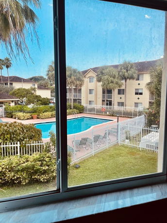 View of a swimming pool area with surrounding buildings seen through a window.