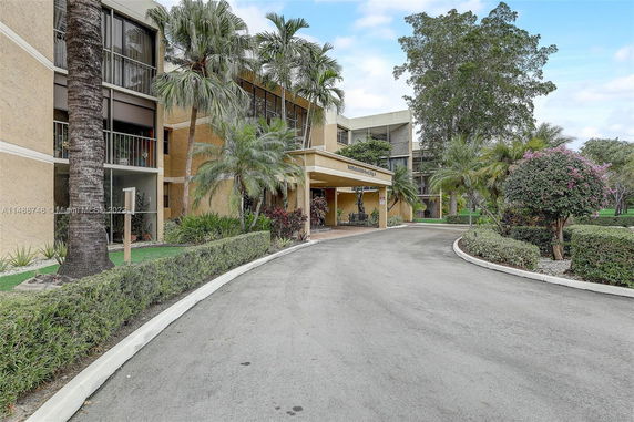 Front view of a multi-story building with a covered entrance and surrounding palm trees.