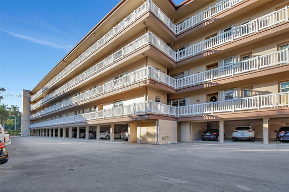 Side view of a multi-story building with balconies and a parking area underneath.