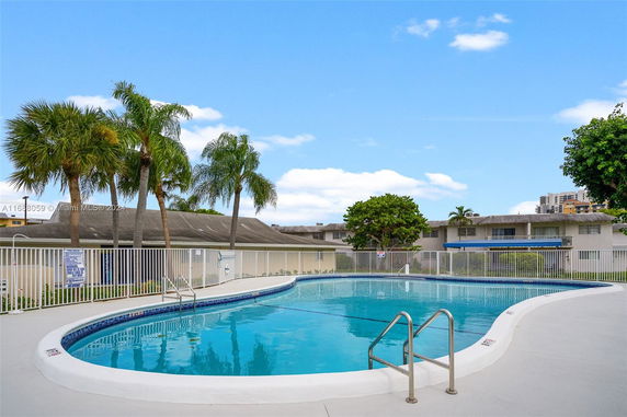 Outdoor swimming pool with surrounding fence and nearby buildings.
