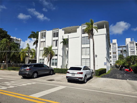 Front view of a multi-story residential building with parking area in front.