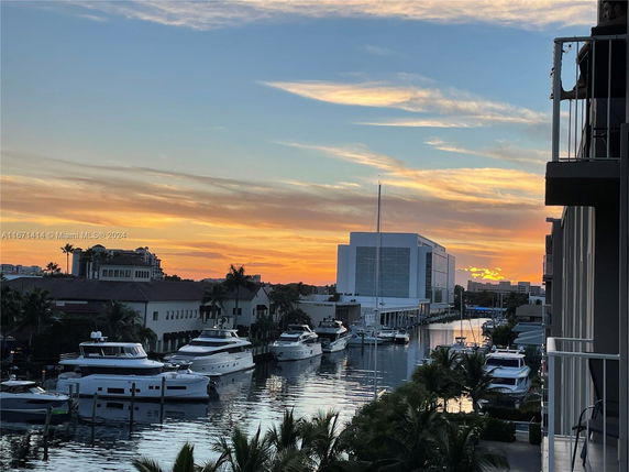 View of yachts docked along a waterfront with a building in the background at sunset.