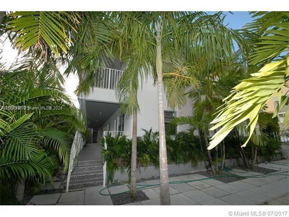 Front view of a two-story building with a staircase and balcony, surrounded by palm trees.