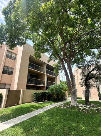 Front view of a multi-story building with balconies and surrounding greenery.
