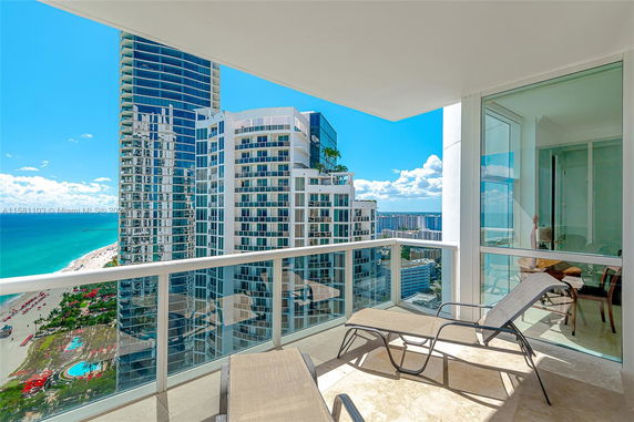 Panoramic view from a building balcony overlooking the ocean and nearby high-rise buildings.