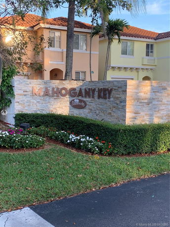 Front view of a residential complex with a decorative stone wall and the name 'Mahogany Key' displayed.