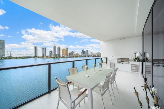 Balcony view of a cityscape with buildings across a body of water, featuring an outdoor dining setup.