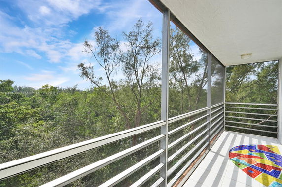 View of surrounding trees from a balcony with railing and tiled floor.