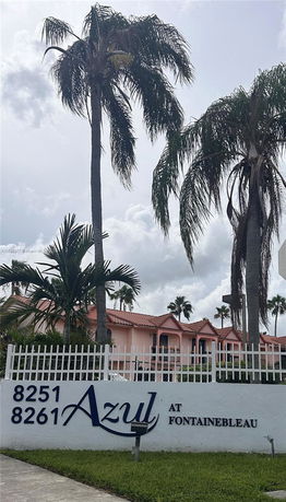 Front view of a residential complex with palm trees and a white fence.