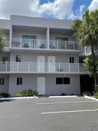 Front view of a multi-story building with balconies and parking area.