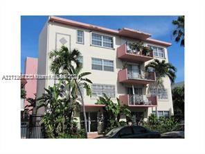 Front view of a four-story apartment building with balconies and tropical plants.