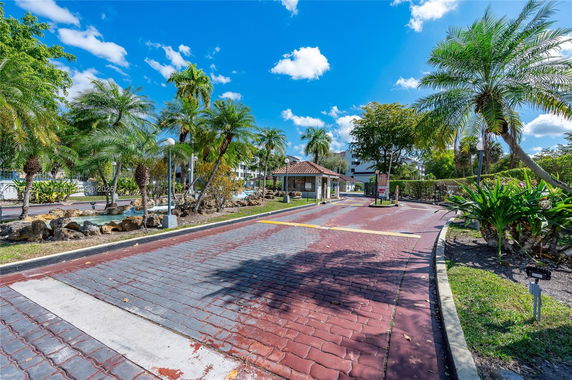 View of a pathway with palm trees and a small building structure in the background.