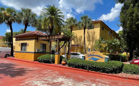Front view of a multi-story building with a small entrance structure and palm trees.