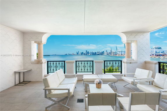 Covered patio with outdoor seating overlooking a body of water and city skyline.