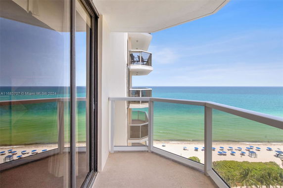 View from a balcony overlooking the ocean and beach with umbrellas.