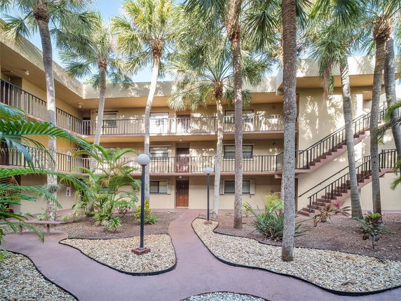 View of a multi-story building with balconies and exterior staircases, surrounded by palm trees.