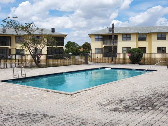 Outdoor swimming pool with surrounding paved area and nearby residential buildings.