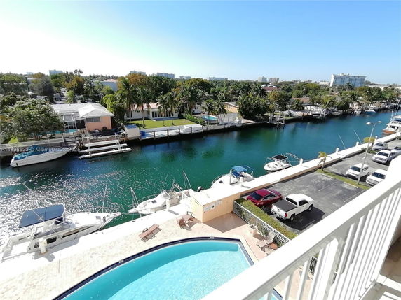Panoramic view from a building showing a swimming pool, parked cars, and a canal with boats.