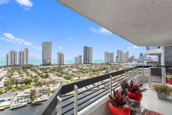 Panoramic view from a high-rise building balcony overlooking a coastal cityscape with tall buildings and the ocean in the background.
