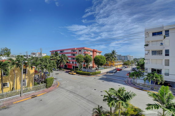 View of street intersection with multi-story buildings and palm trees.