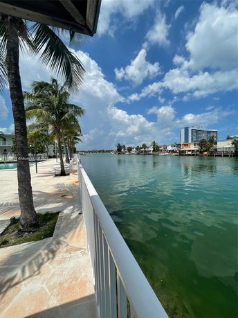 View of a waterfront area with palm trees and buildings across the water.