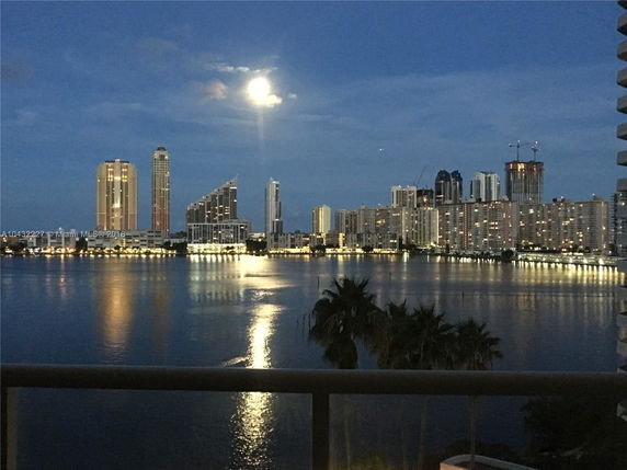 Panoramic view of a cityscape at night with tall buildings and their reflections on the water.