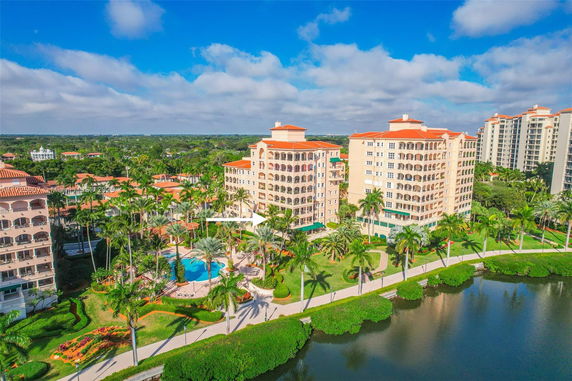 Aerial view of multiple multi-story residential buildings with red roofs, surrounded by palm trees and a swimming pool.