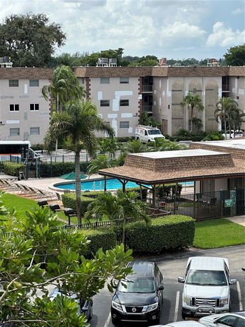 View of a building complex with a swimming pool and parking area in the foreground.