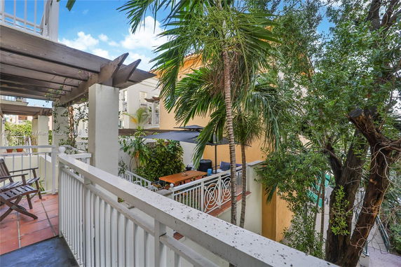 View from a balcony overlooking a patio area with trees and nearby buildings.