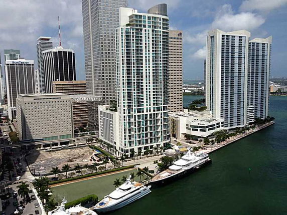Aerial view of several high-rise buildings near a body of water with yachts docked nearby.