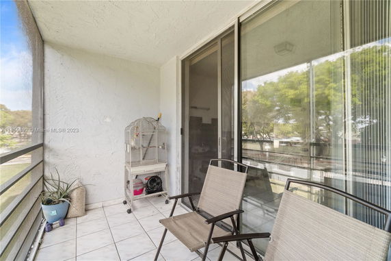 Balcony area with two chairs and a birdcage, overlooking outdoor surroundings.