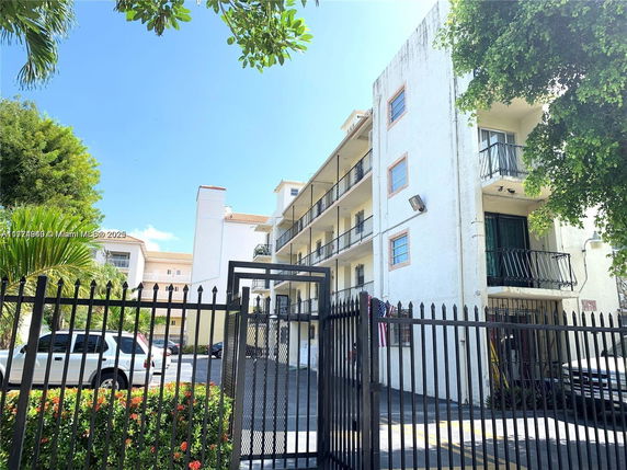 Front view of a multi-story apartment building with balconies and gated entry.