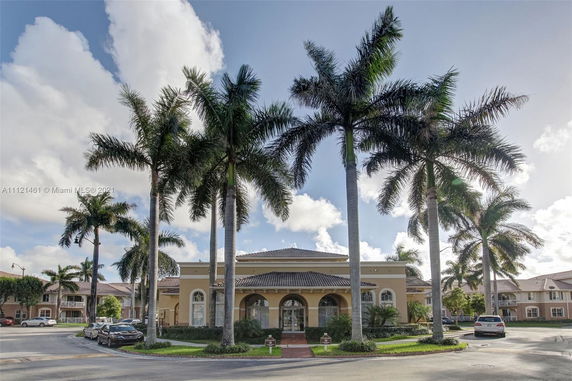 Front view of a building with a tiled roof and large arched windows, surrounded by palm trees.
